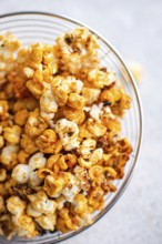 Top view of a glass bowl overflowing with caramel-coated popcorn, showcasing a mix of golden hues
