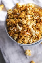 Top view of a bowl filled with crunchy caramel popcorn on a textured cloth background