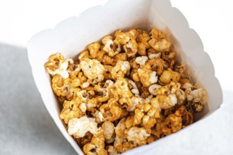 Top view of delicious caramel-coated popcorn filling a white paper container, showcasing a range of