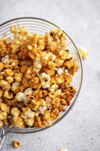 Top view of a glass bowl overflowing with crunchy caramel popcorn, staged on a soft gray background