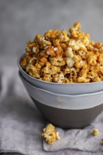 Gray bowl filled with crunchy, sweet caramel popcorn, placed on a soft-textured gray cloth