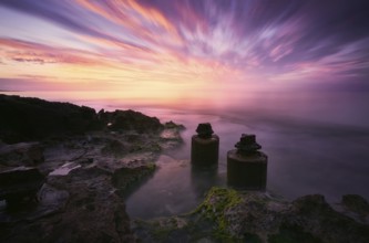 A mesmerizing sunset with vibrant hues reflecting over calm waters, coastal rocks, and ancient