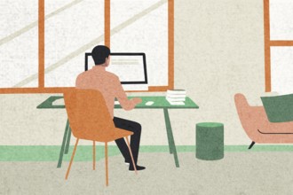 A man sits at a green desk in a light-flooded room, focused on his computer Books are stacked