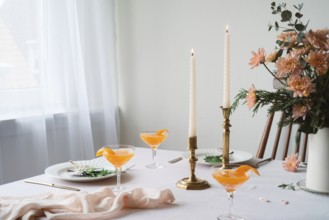 An elegantly set table featuring refreshing Mandarin drinks, lit beeswax candles, intricate floral