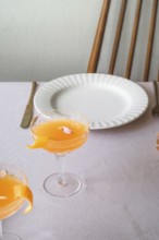 A well-appointed dining table featuring a bright mandarin drink in a sophisticated glass,