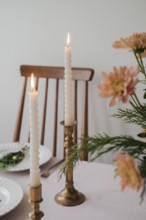 A serene dinner table setup featuring two lit taper candles in brass holders, complemented by fresh