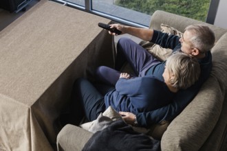 A senior couple sits closely on a comfortable couch, sharing a peaceful moment watching TV