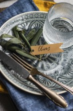 Sophisticated table setting featuring olive leaves on a ceramic plate with a tag, accompanied by a
