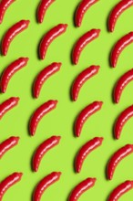 Vibrant, glossy red plastic peppers on a bright green background symbolize artificiality in diet