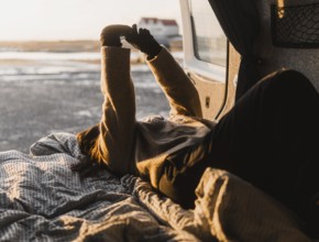 Unrecognizable woman lounging in a van during a camping trip in Iceland. She stretches her arms