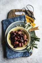 Top view of a ceramic bowl filled with Greek BBQ olives. The setting includes rustic kitchen
