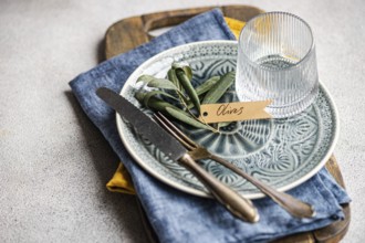 Sophisticated table setting featuring olive leaves on a ceramic plate with a tag, accompanied by a