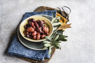 Ceramic bowl filled with Greek BBQ olives, served alongside fresh olive leaves and a rustic denim