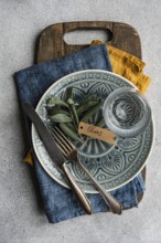 Top view of olive leaves artistically on ornate tableware. A rustic wooden board, vintage cutlery,