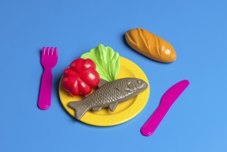 A colorful display with plastic toy food on a plate, including fish, bread, and vegetables,
