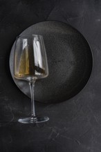 From above, an elegant glass of dry white wine placed carefully on a textured black plate,