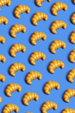 Brightly colored plastic croissants on a vibrant blue background, symbolizing the critique of