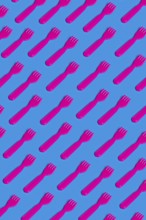 Rows of pink plastic cutlery on a blue background symbolizing the artificiality and environmental