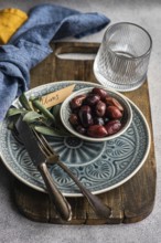 A tasteful arrangement of Greek BBQ olives on a ceramic plate, accompanied by a glass, rustic