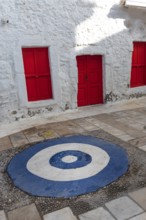 Bright red doors and white wall of typical traditional architecture with a blue and white symbol to