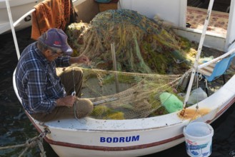 Bodrum, Mugla, Turkey. April 23rd 2022 A fisherman mending nets on his boat in Bodrum town harbour,