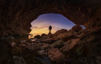 A stunning silhouette of a person standing on rocky terrain under a vibrant sunset sky, viewed from