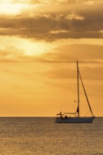 A serene view of a sailboat gliding across calm waters at sunset, surrounded by golden skies,