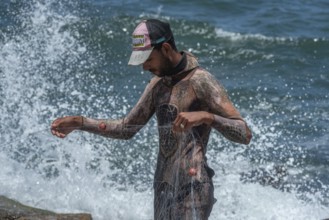 An young Egyptian fisherman wearing a wetsuit arranges his net on the Mediterranean Sea front of