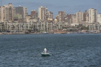 A lone Egyptian fishermen in a small boat fishing in the Mediterranean sea with the skyline of