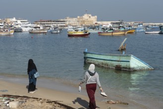 Alexandria, Egypt. December 1st 2022 Two Muslim women walk on the beach near a sunken boat in front