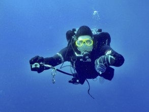 A diver with complete diving equipment extends the second controller to his dive partner, who has