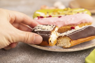 Glazed Eclairs on brown concrete background and green linen textile with hand, cup of coffee, side