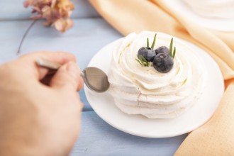 Pavlova Meringue dessert with crisp meringue and blueberry with hand on blue wooden background with