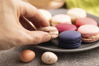 Macarons colourful cookies dessert with hand on brown concrete background with green linen textile,