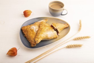 Triangles Pie, Puff Pastry, Samsa with cherry jam on white wooden background, cup of coffee, side
