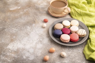 Macarons colourful cookies dessert, cup of coffee, on brown concrete background with green linen