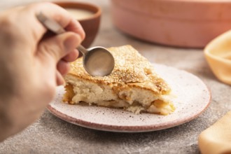 Apple Charlotte cake with hand on brown concrete background and orange linen textile, cup of milk,