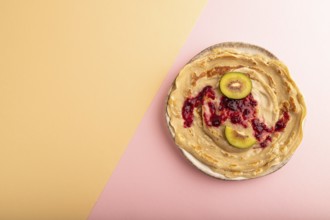 Stack of Plain Fried pancakes with jam and kiwi on pink and orange pastel paper background. top