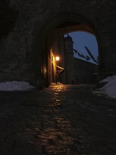 View of the courtyard of Rosenberg Fortress through a medieval archway, illuminated at night,