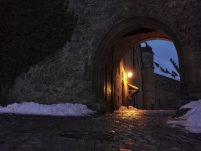 View of the courtyard of Rosenberg Fortress through a medieval archway, illuminated at night,