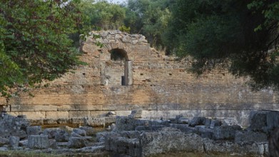 Palestra, red brick wall with an arch surrounded by vegetation and ruined architecture,