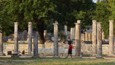 Palestra, Man Walking Between Ancient Columns, Surrounded by Green Trees and Ruined Architecture,