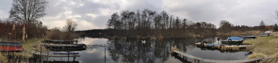 A calm lake with jetties and boats, surrounded by barren vegetation and clear skies, Berlin
