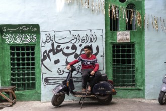 Cairo, Egypt. April 15th 2025. A young Egyptian man sits on a motor scooter outside a brightly