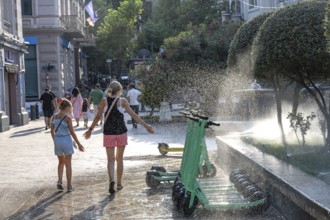 Tbilisi, Georgia. July 29th 2025. A woman and child enjoy the cool spray of a garden sprinkler in
