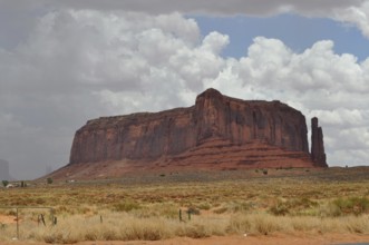 Huge rock in a wide desert landscape with cloudy sky in the background, Monument Valley, Navajo