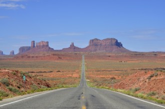 The long, straight road runs through a desert-like landscape with rocks. Access to Monument Valley,