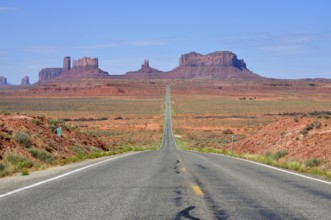 Straight road leads endlessly through a vast desert landscape with rocks in the background,