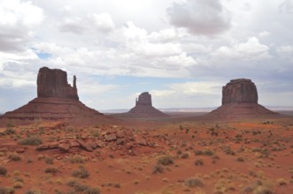 Monument Valley with distinctive rock formations and sparse vegetation under cloudy sky, Monument