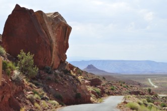 Large rock juts out next to a road in a vast desert landscape, Monument Valley, Navajo Tribal Park,
